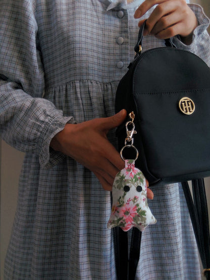 front view of pink floral upcycled ghost keychain displayed on purse held by model