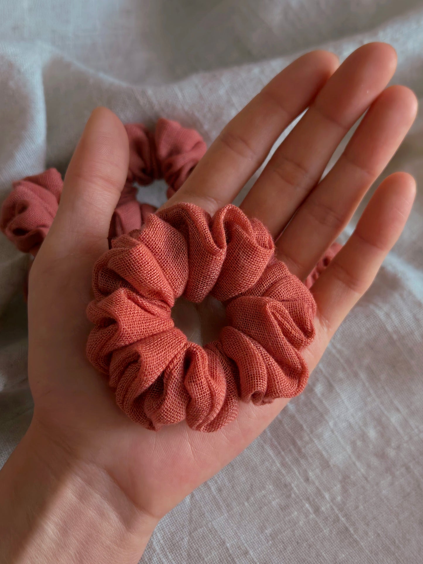 front view of terracotta linen upcycled scrunchie in hand size reference